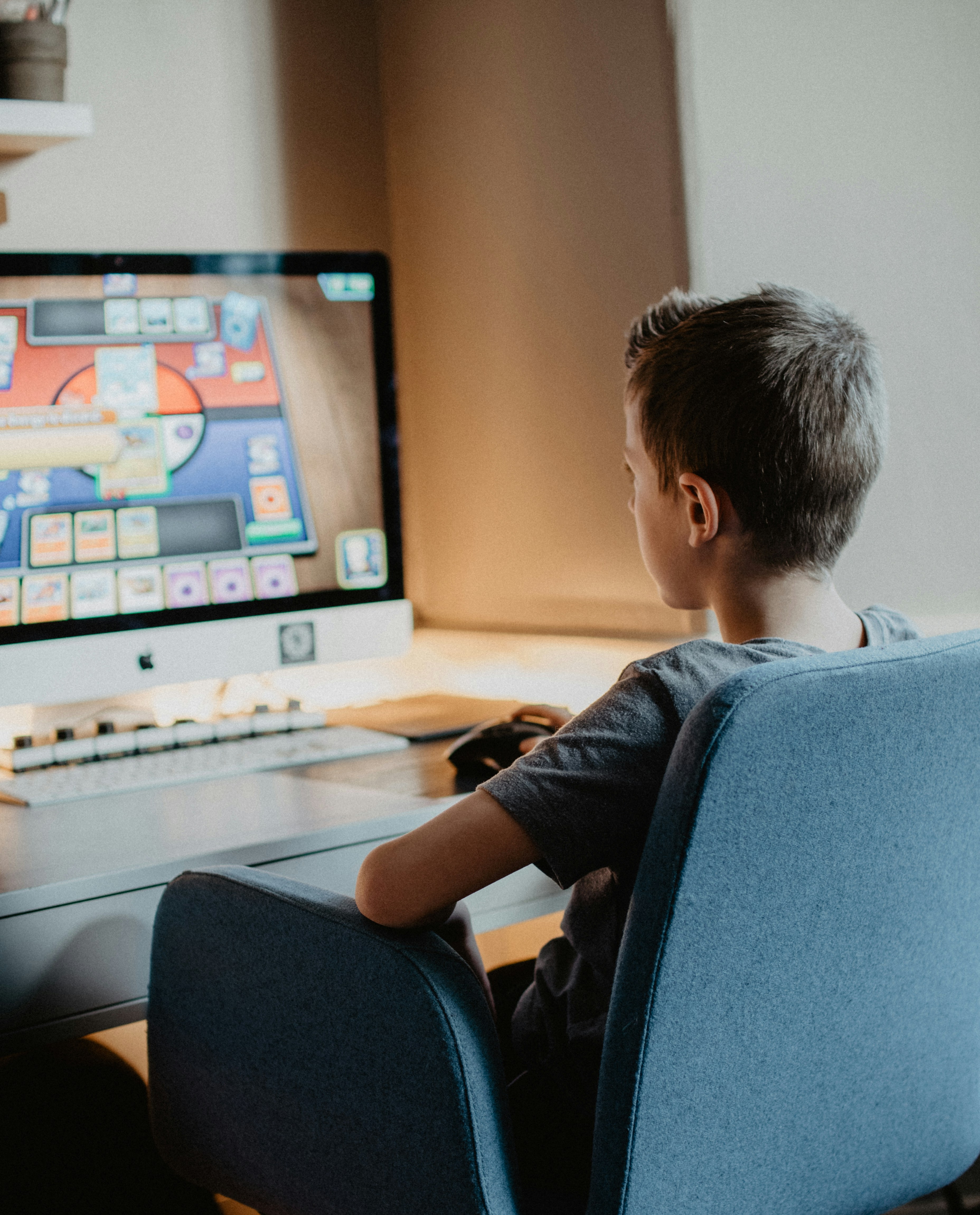 Young boy playing Pokemon on home computer by Learning Game boy in black long sleeve shirt sitting on blue chair